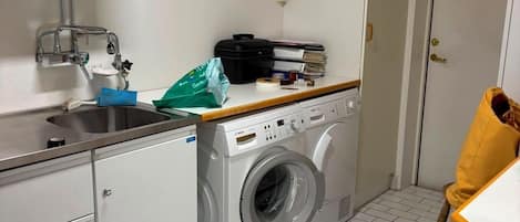 A compact laundry room with a washing machine, a sink, and a window.