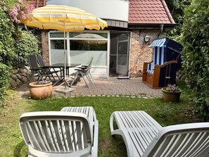 A patio area with outdoor furniture, a yellow umbrella, and a brick building with a glass door. - Süderstraße 29a, Apt. 01 - Spacious 3-room vacation apartment with a terrace and (Sylt)