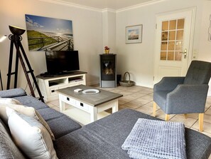 A living room with a sofa, a coffee table, a television, a fireplace, and a door with glass panels. - Süderstraße 29a, Apt. 01 - Spacious 3-room vacation apartment with a terrace and (Sylt)