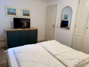 A bedroom with a bed, a dresser, a television, and two framed pictures on the wall. - Süderstraße 29a, Apt. 01 - Spacious 3-room vacation apartment with a terrace and (Sylt)