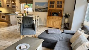 A modern kitchen with a dining area, a grey sofa set, and a wooden cabinet with a radio. - Süderstraße 29a, Apt. 01 - Spacious 3-room vacation apartment with a terrace and (Sylt)