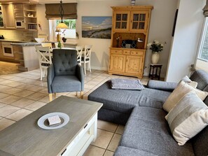 A modern kitchen with a dining area, a grey sofa set, and a wooden cabinet with a radio. - Süderstraße 29a, Apt. 01 - Spacious 3-room vacation apartment with a terrace and (Sylt)