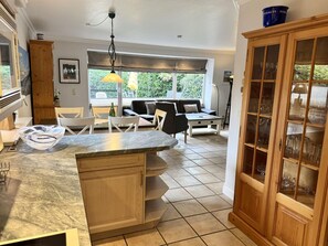 A kitchen with a marble countertop, wooden cabinets, a dining area with a sofa, and a window with curtains. - Süderstraße 29a, Apt. 01 - Spacious 3-room vacation apartment with a terrace and (Sylt)