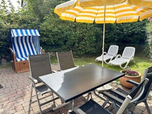 Eine Terrasse im Freien mit Tisch und Stühlen, einem gestreiften Sonnenschirm und einem überdachten Sitzbereich.