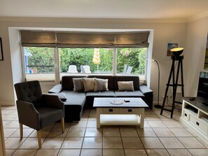 Ein Wohnzimmer mit Ecksofa, Couchtisch, Sessel, Stehlampe und Fernseher.