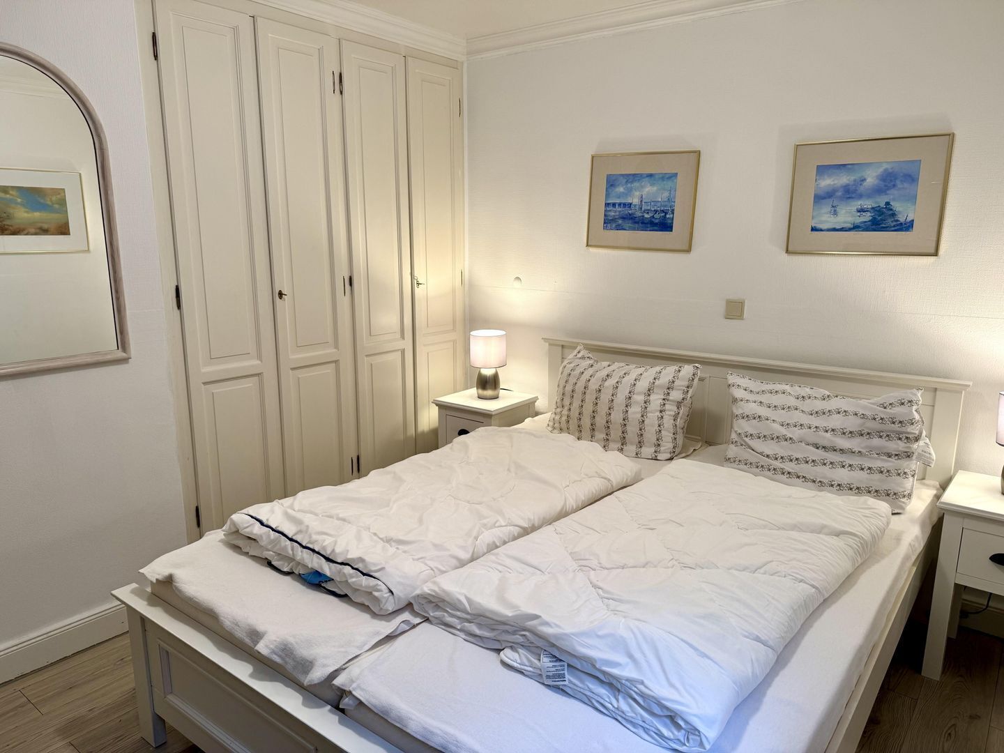 Una cama bien hecha con ropa de cama blanca y almohadas estampadas, una mesita de noche con lámpara y un armario con espejo.