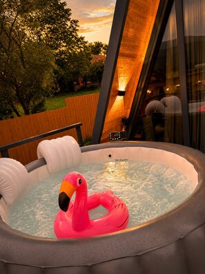 A hot tub with a pink flamingo float, surrounded by a wooden deck and a glass enclosure.