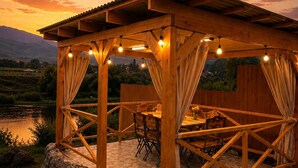 A wooden outdoor pavilion with a tiled floor, surrounded by a natural landscape and a body of water. - A-frame with lake view near Stepanavan (Vardablur)