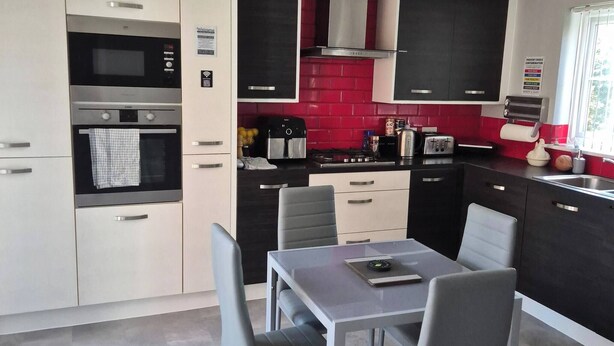 Una cocina moderna con electrodomésticos integrados, una zona de comedor con mesa y sillas, y un protector contra salpicaduras rojo.