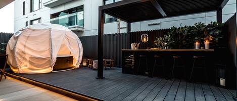 Un espace extérieur aménagé avec un coin salon, un jacuzzi couvert, des tabourets de bar et une terrasse en bois.