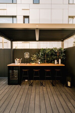 A covered outdoor bar area with a wooden table, bar stools, a wine cooler, and a large potted plant. - Urban Deluxe Igloo Jacuzzi Terrace (București)