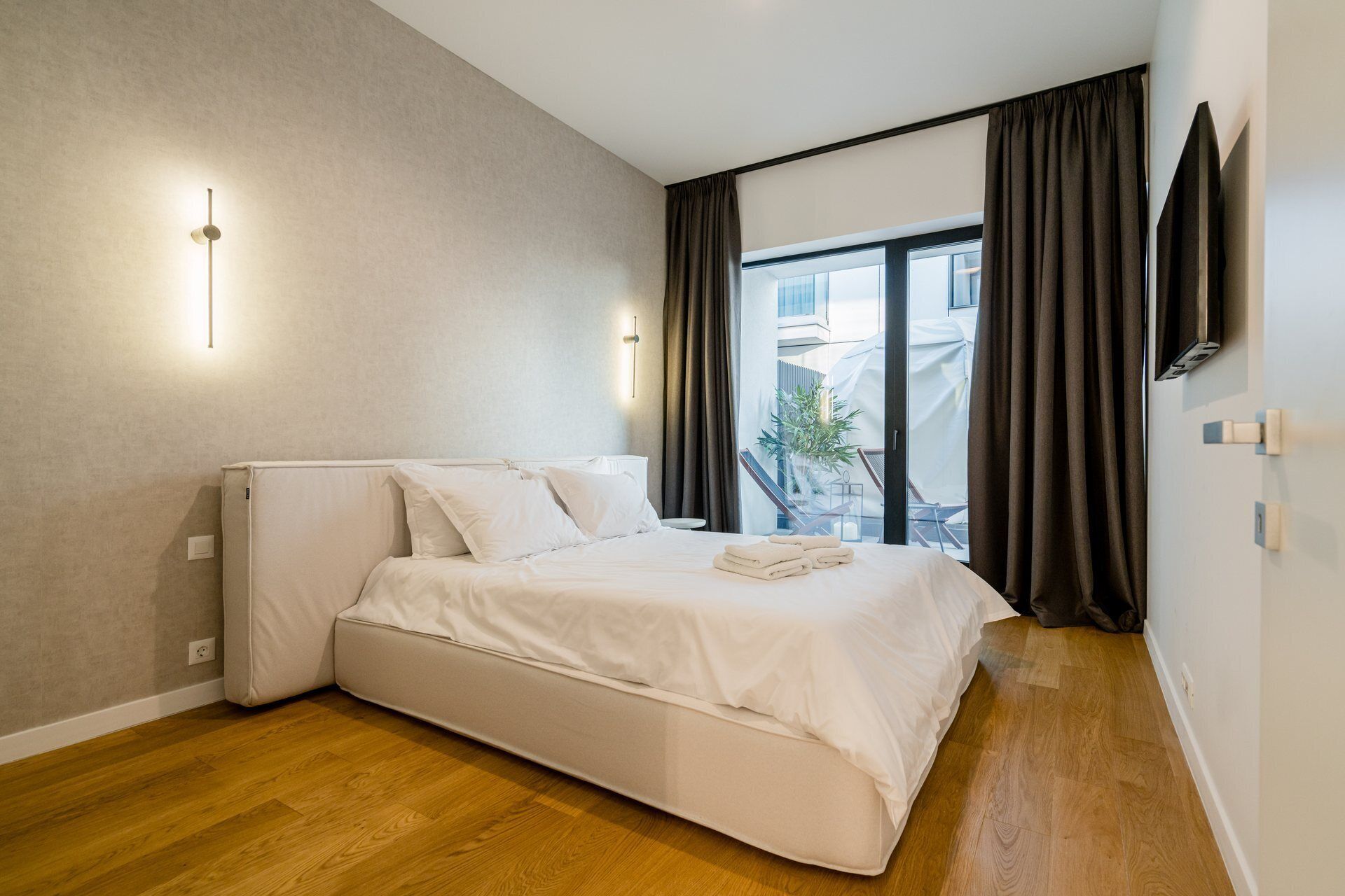 Un dormitorio moderno con cama, televisor de pantalla plana y ventana con cortinas.