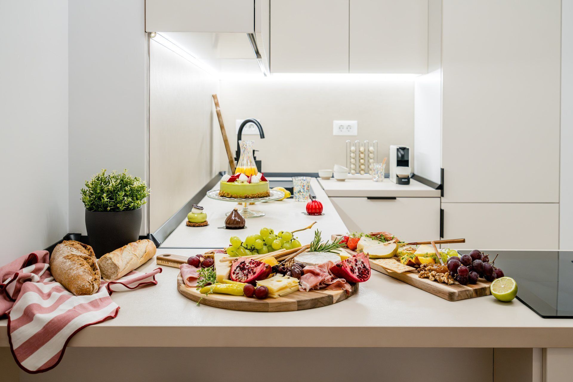 A kitchen counter with a variety of food items including bread, cheese, fruits, and a cake.