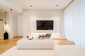 A modern living room with a flat-screen TV mounted on the wall, a white ottoman with magazines, and a minimalist design. - Urban Deluxe Igloo Jacuzzi Terrace (București)