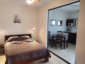 A bedroom with a bed, a desk, and a kitchenette in the background. - Marina Loft #103, 1 floor (Playa Del Coco)