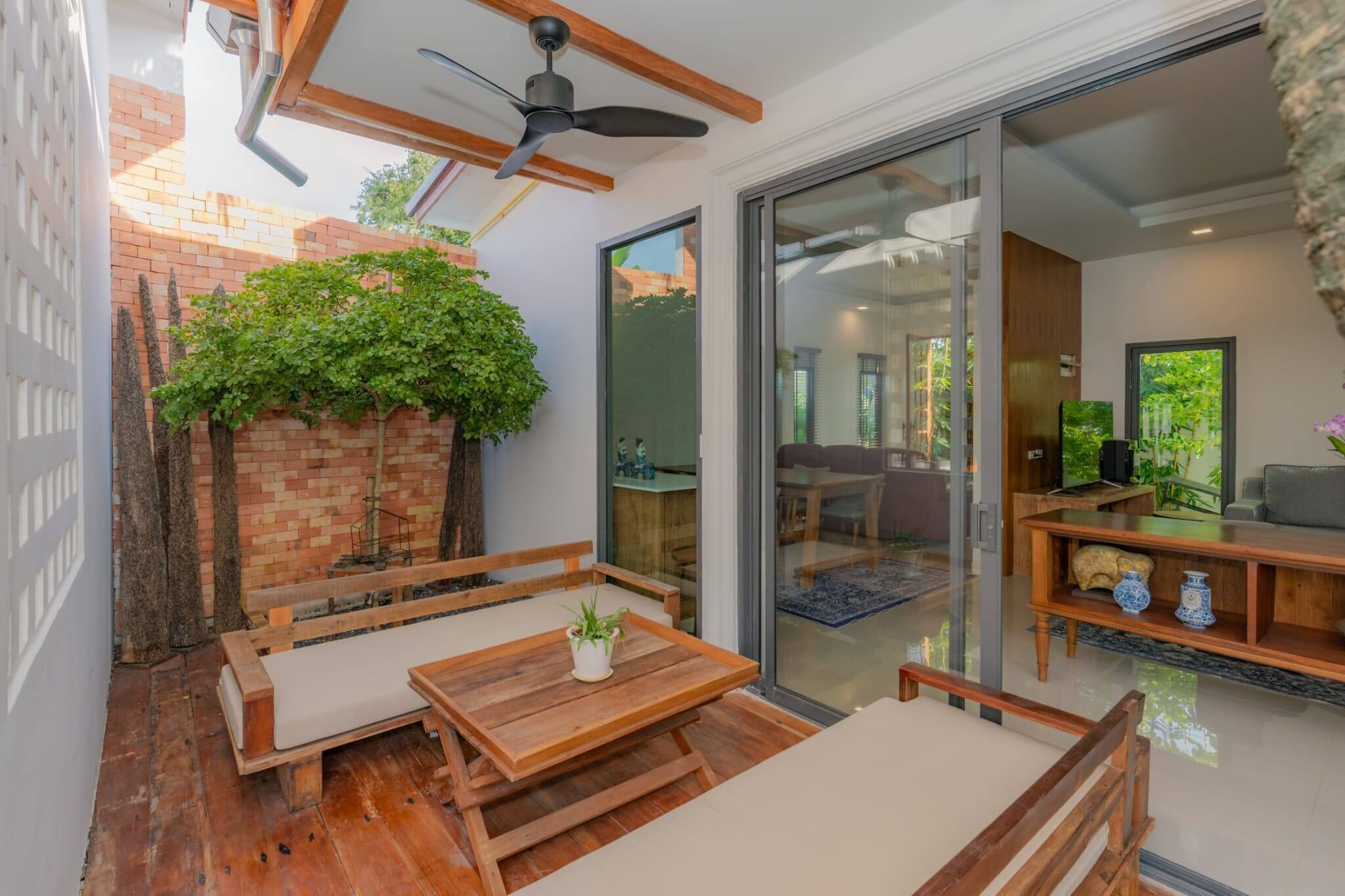 Eine Terrasse mit Holzmöbeln, einem Deckenventilator und einer Ziegelwand mit Pflanzen.