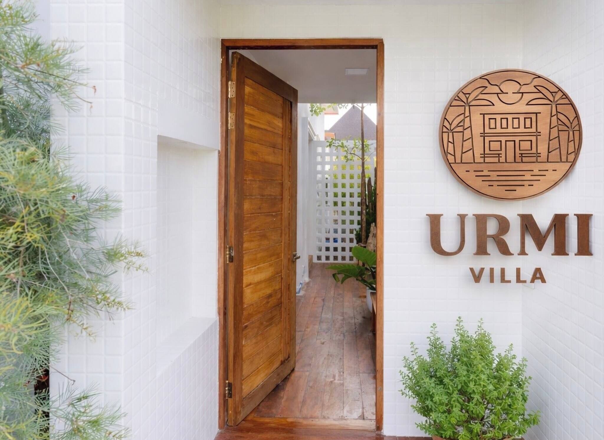 Puerta de madera que da a un pasillo con pared de azulejos blancos y un letrero que dice 'URMI VILLA'.