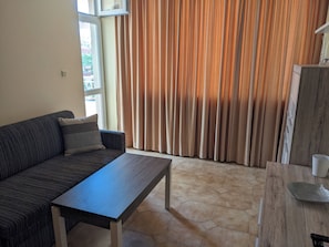A living room with a sofa, a coffee table, a cabinet, and a window with curtains.
