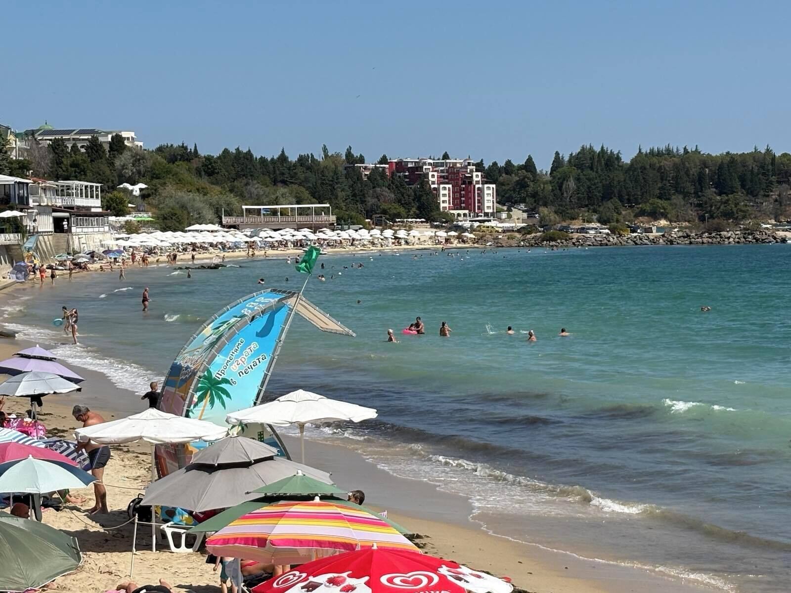 Una playa con sombrillas, gente y un edificio al fondo.