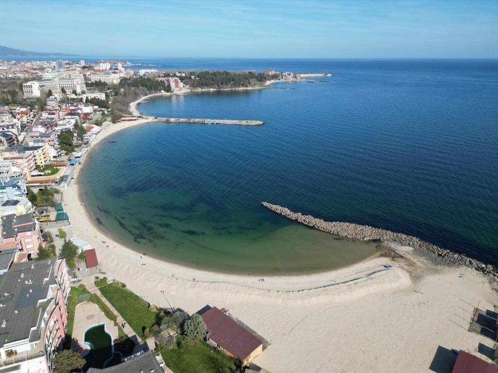 A coastal town with a sandy beach, a rocky breakwater, and residential buildings.