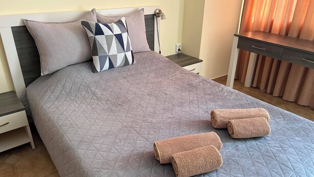 A neatly made bed with a geometric patterned bedspread, two pillows, and two rolled towels on the bed. - Komfortables Apartment mit 2 Schlafzimmern direkt am Strand in Nessebar (Nesebar)