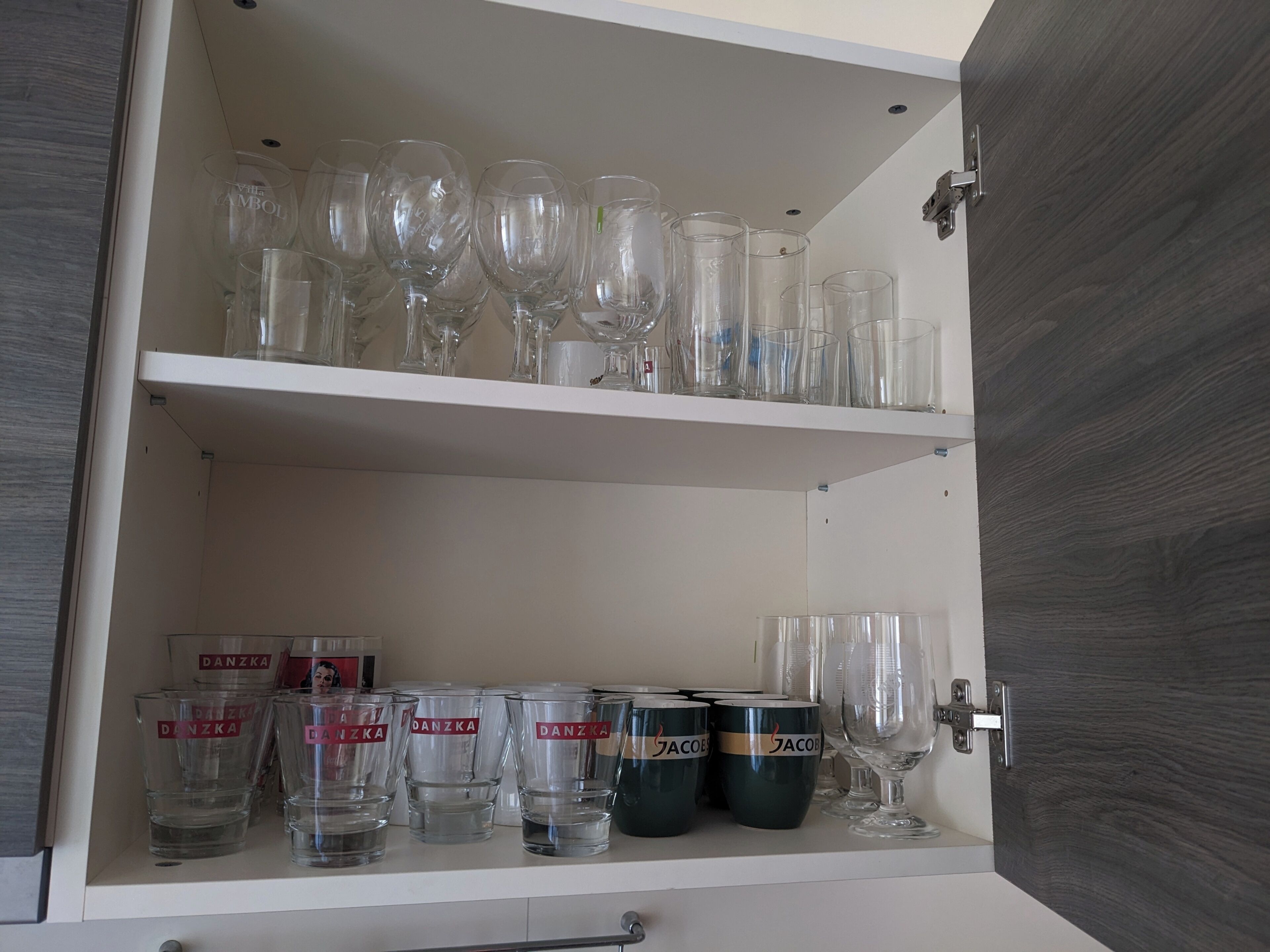A cabinet with shelves holding various glassware, including wine glasses and tumblers.