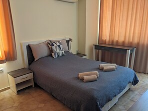 A neatly made bed with a dark blue blanket and two pillows, a small bedside table with a drawer, and a wooden nightstand.