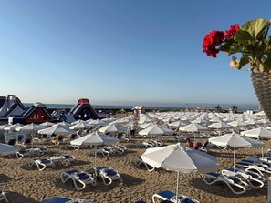 Ein Strand mit vielen weißen Sonnenschirmen und Liegestühlen zum Sonnenbaden.