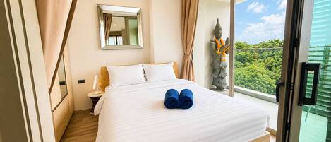 A hotel room with a large bed, a mirror, a statue, and a view of greenery.