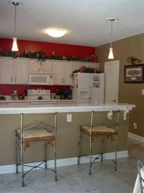 A kitchen with white cabinets, a microwave, and a refrigerator. There are two metal bar stools with cushions. - Right at Lake Tobesofkee & 10 miles from downtown! (Macon)