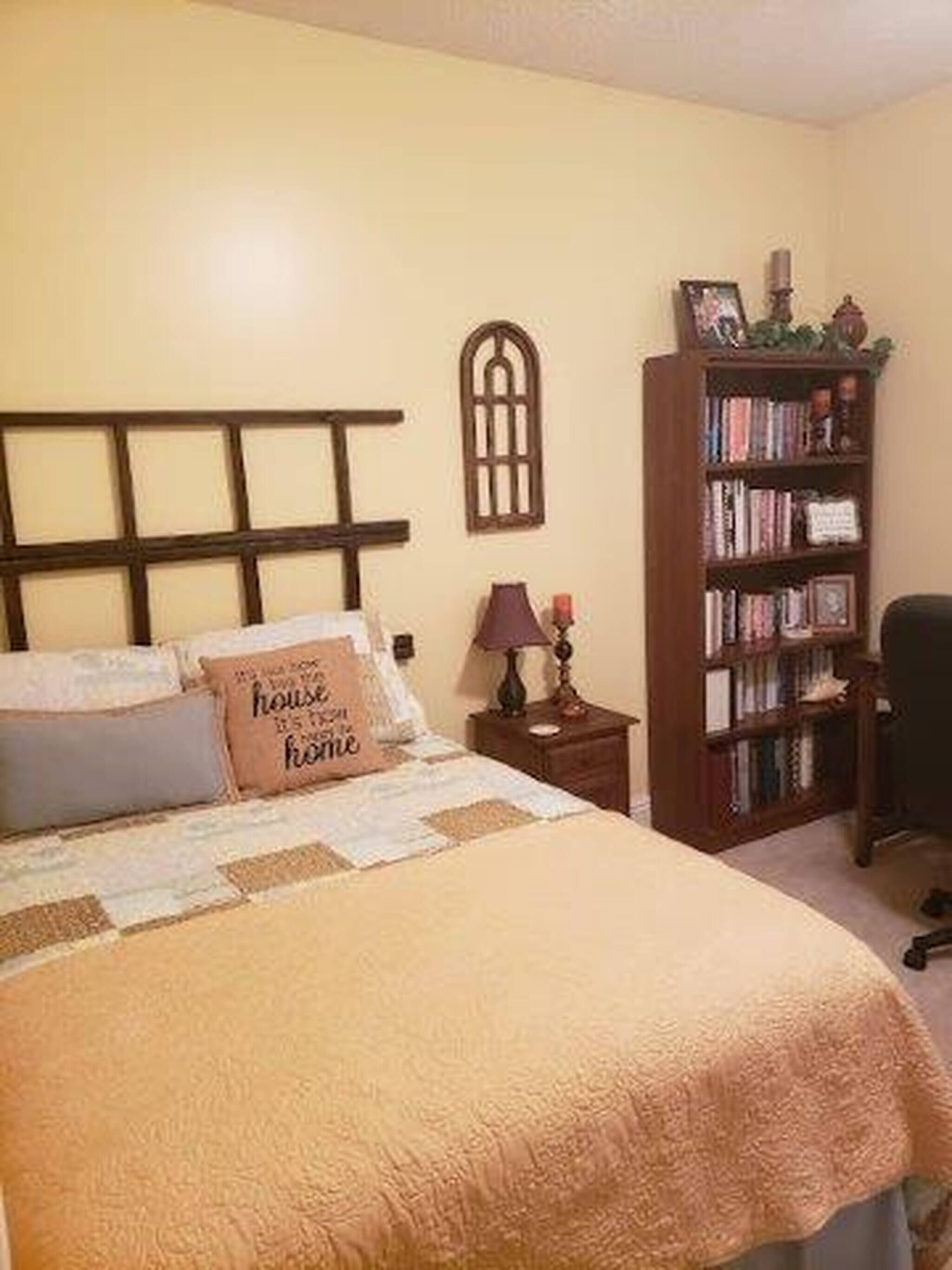 Een slaapkamer met een bed, nachtkastje, boekenplank en raam.