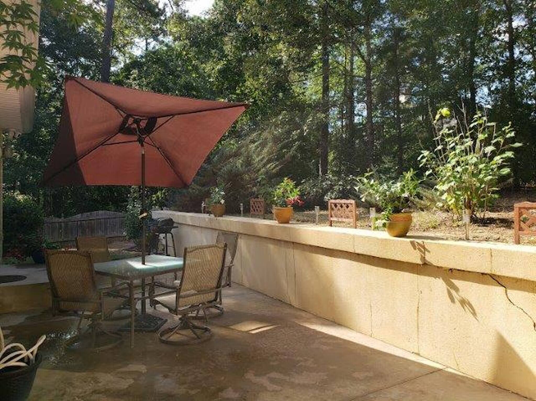Ein Terrassenbereich im Freien mit Tisch, Stühlen, einem großen Sonnenschirm und Kübelpflanzen.