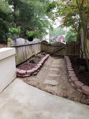 Un giardino con un vialetto in cemento, una recinzione in legno e un cordolo in mattoni.
