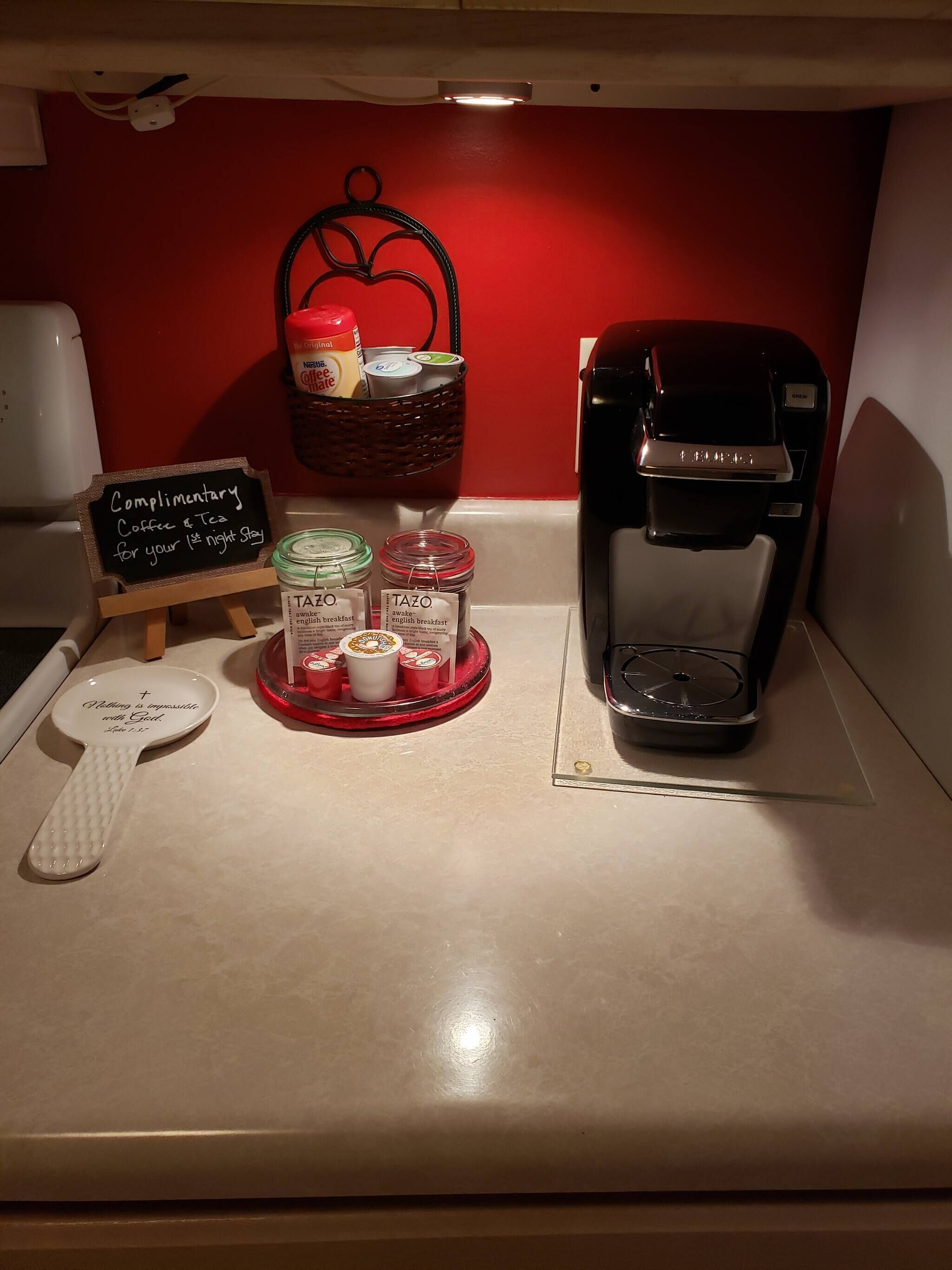 Estación de café con cafetera, una cesta de bocadillos y un cartel que ofrece café y té de cortesía.