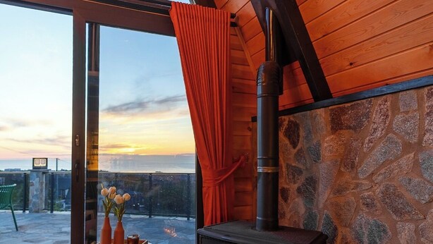 Una habitación acogedora con pared de piedra, chimenea y vista al atardecer.