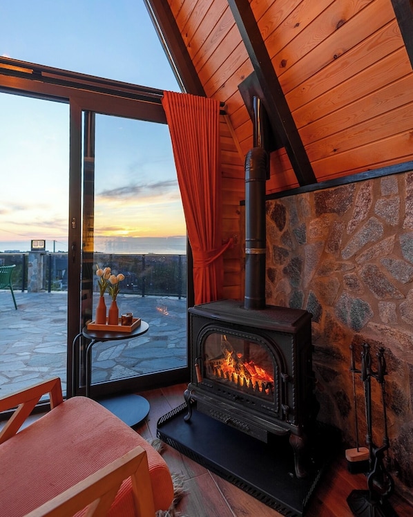 A cozy room with a stone wall, a fireplace, and a view of the sunset. - Koda bungalov (Ardeşen)