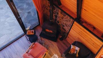 Ein Holzblockhaus-Interieur mit Kamin aus Stein, einer Couch, einem Sessel und einem kleinen Tisch mit Blumen in einer Vase.