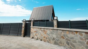 Un edificio de techo inclinado, paredes de piedra y una valla metálica.