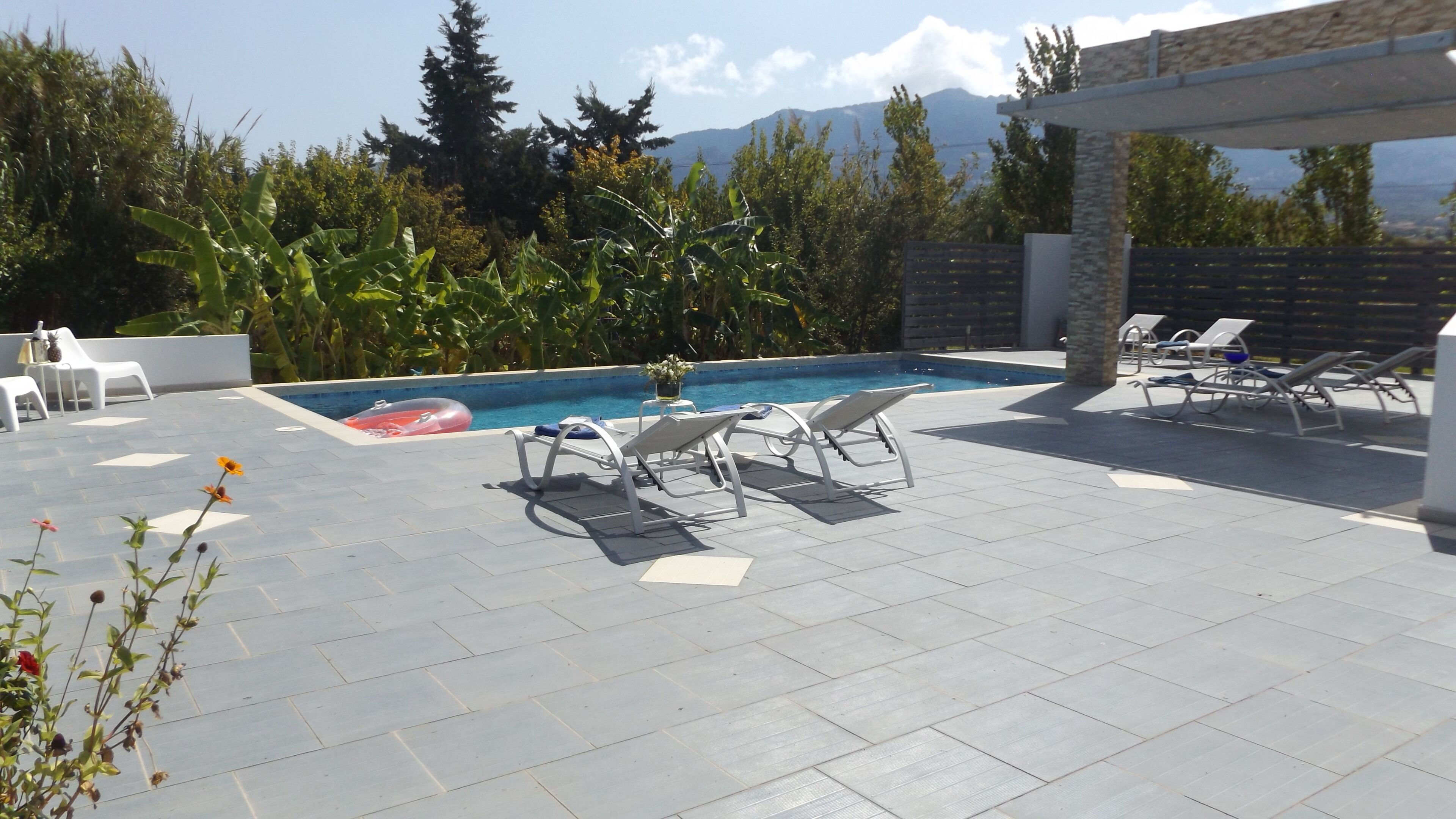 A pool area with lounge chairs, a hot tub, and a view of mountains.