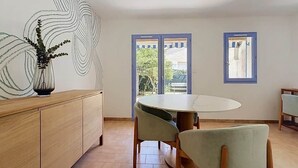 A dining area with a round table and chairs, a wooden cabinet, and a wall with a unique design. - A charming little house near Lake Salonique. (Le Grau-du-Roi)