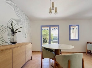 A dining area with a round table and chairs, a wooden cabinet, and a wall with a unique design. - A charming little house near Lake Salonique. (Le Grau-du-Roi)