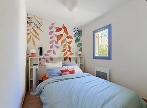 A bedroom with a bed, a radiator, a window, and a wall with leaf patterns. - A charming little house near Lake Salonique. (Le Grau-du-Roi)