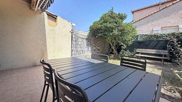 A patio with a table and chairs, a wooden fence, and a tree. - A charming little house near Lake Salonique. (Le Grau-du-Roi)