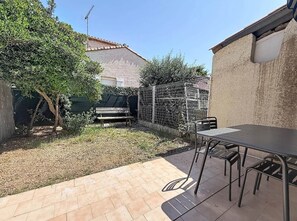 Eine Terrasse mit Tisch und Stühlen, ein eingezäunter Garten und ein Gebäude im Hintergrund.