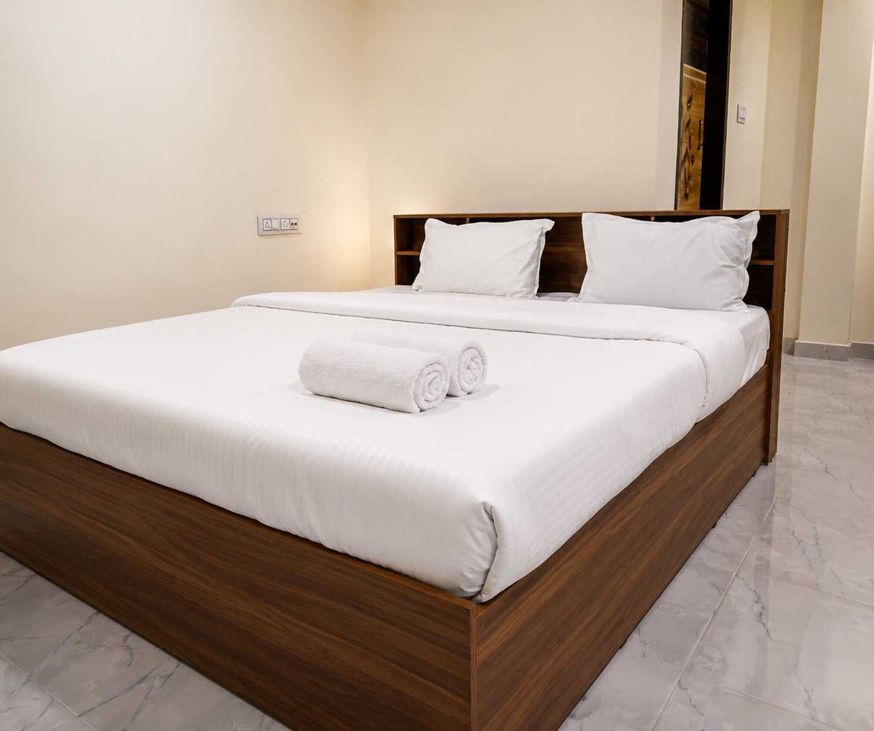 Una cama bien hecha con sábanas blancas y una toalla enrollada, un cabecero de madera y un suelo de mármol.