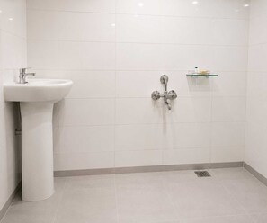 Un baño moderno con un lavamanos pedestal, una ducha con repisa de vidrio y desagüe en el piso.