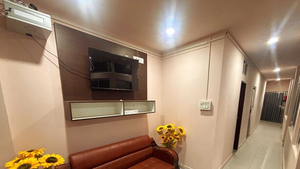 A hallway with a brown leather sofa, a flat-screen TV mounted on the wall, and a vase with sunflowers.