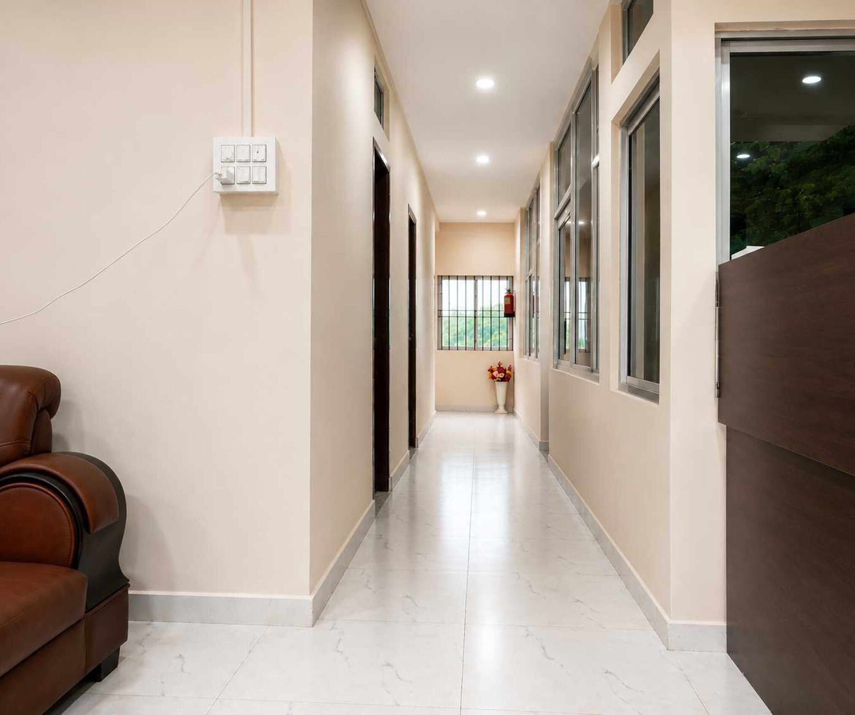 A hallway with a brown leather sofa, a white tiled floor, and a window with a view of greenery.