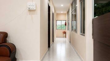 A hallway with a brown leather sofa, a white tiled floor, and a window with a view of greenery.