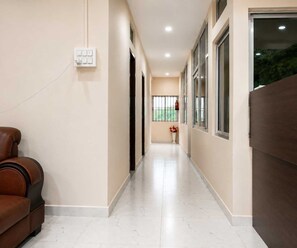 A hallway with a brown leather sofa, a white tiled floor, and a window with a view of greenery. - Classic Hayat Hill Top (Guwahati)